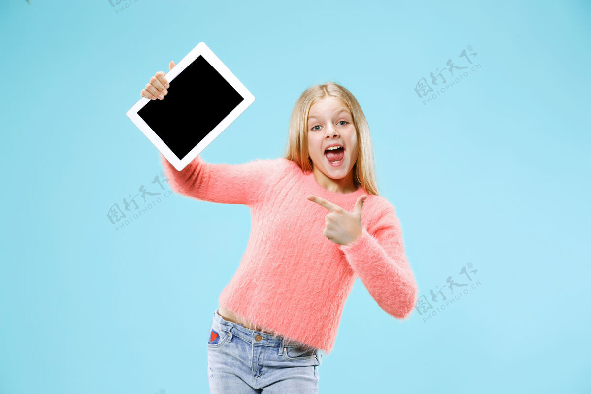 休闲在蓝色画室背景上拿着平板电脑的有趣的小女孩她展示了一些东西并指着屏幕学习电脑童年