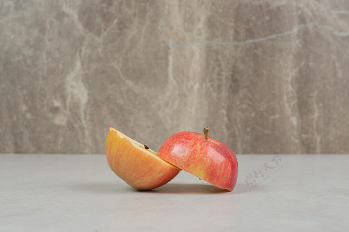成熟灰色桌子上有两个半切的红苹果切片半份剁碎