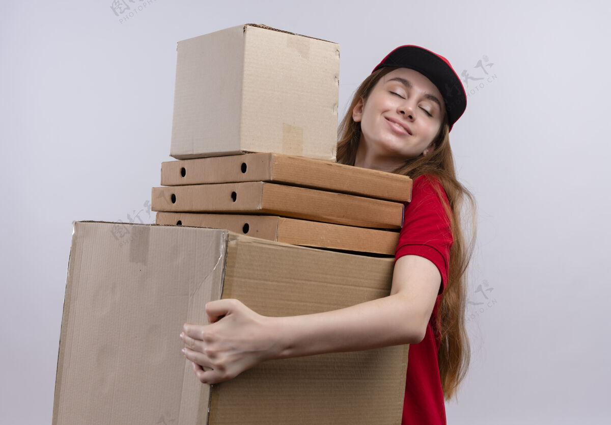 红色穿着红色制服的年轻送货女孩高兴地拿着箱子和包裹 站在与世隔绝的白色空间里制服送货箱子