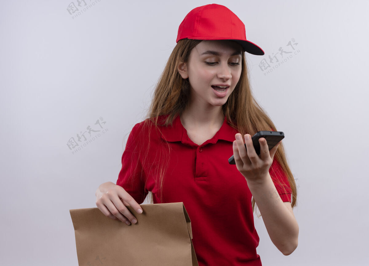印象印象深刻的年轻送货女孩在红色制服举行 并在孤立的白色空间看手机送货手持年轻