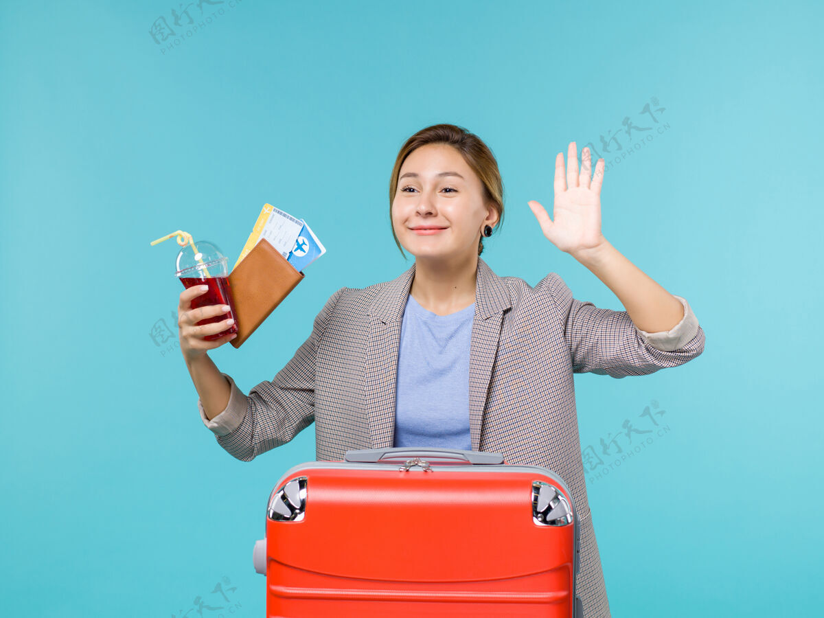假期正面图度假中的女性手持果汁和机票在蓝色背景上向某人挥手旅行度假海上飞机举行旅行成人