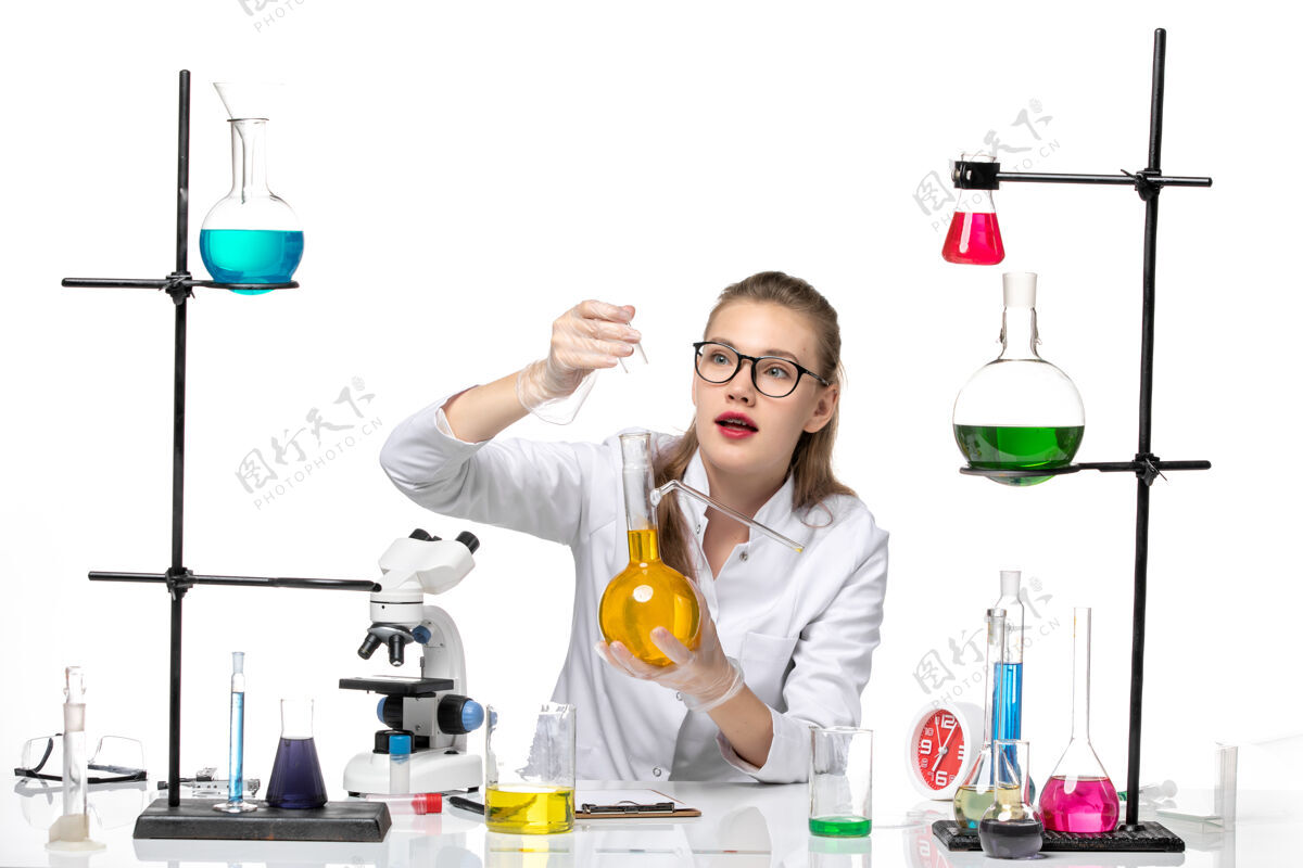 药正面图：穿着医疗服的女化学家拿着白色桌子上的黄色溶液烧瓶化学大流行性冠状病毒化学持有高尔夫