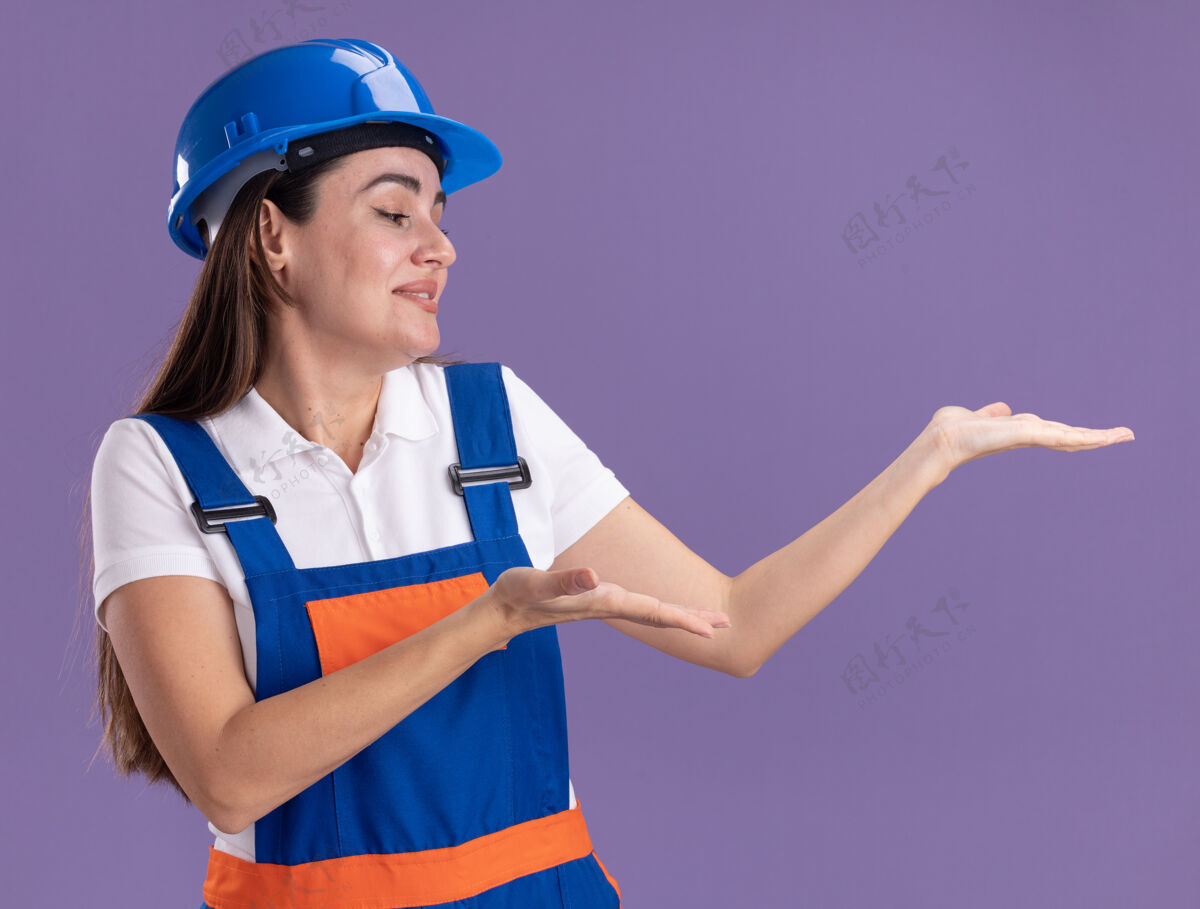 人一个穿着制服的年轻建筑女假装拿着一个孤立的东西在紫色的墙上复制空间假装女人人