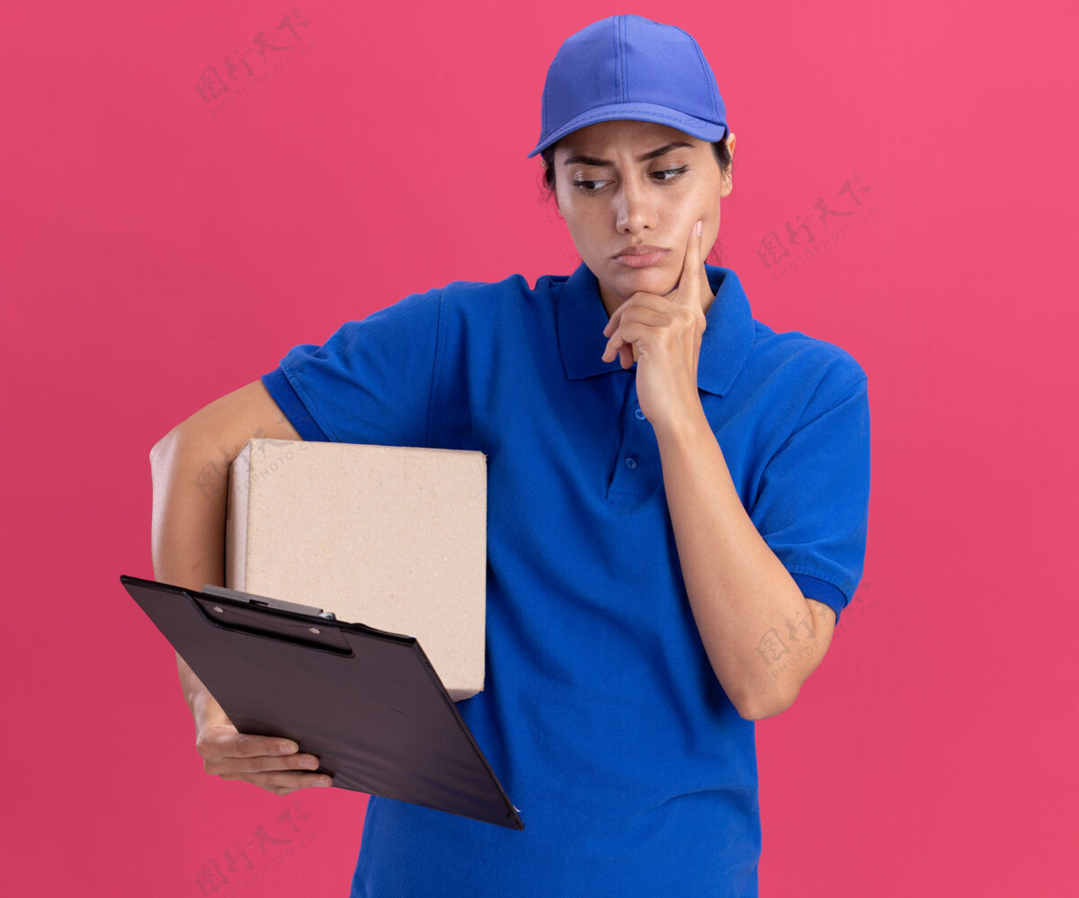 表情想着那个穿着制服 拿着帽子盒的年轻送货女孩 看着手里的剪贴板 把手指放在隔离在粉红色墙上的脸颊上感觉脸颊盒子