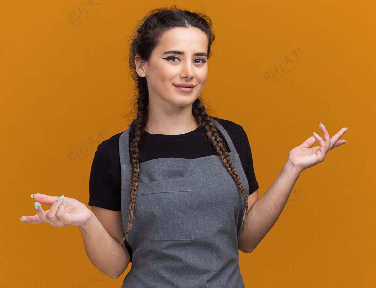 制服高兴的年轻女理发师穿着制服摊开双手孤立在橙色的墙上脸理发师女性