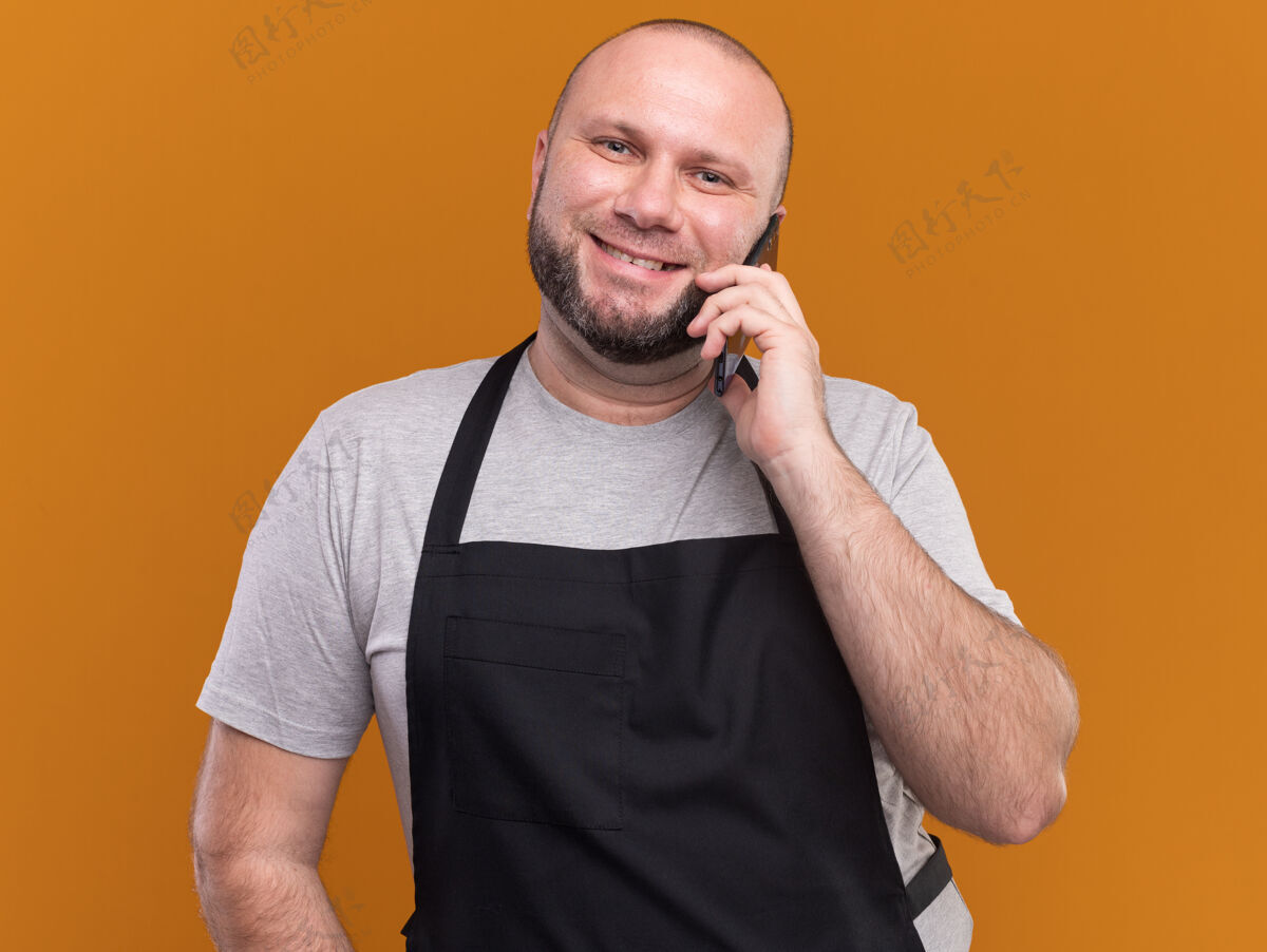 理发师身着制服 面带微笑的斯拉夫中年男理发师在橙色墙壁上讲电话人人感觉