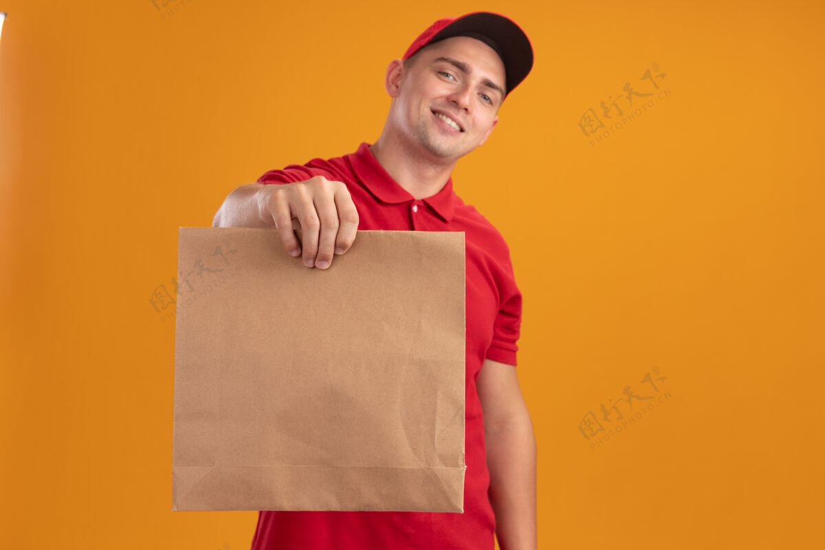 衣服笑容满面的年轻送货员身穿制服 戴着帽子 在橘黄色的墙壁上 把纸食品包举在前面人感觉人
