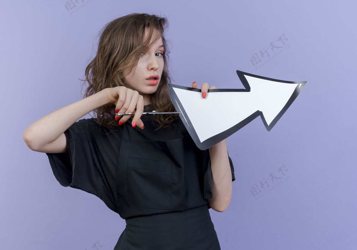 标记自信的年轻斯拉夫女理发师穿着制服 手里拿着剪刀和箭标 这是指在一边试图切断箭标孤立的紫色背景剪试试年轻