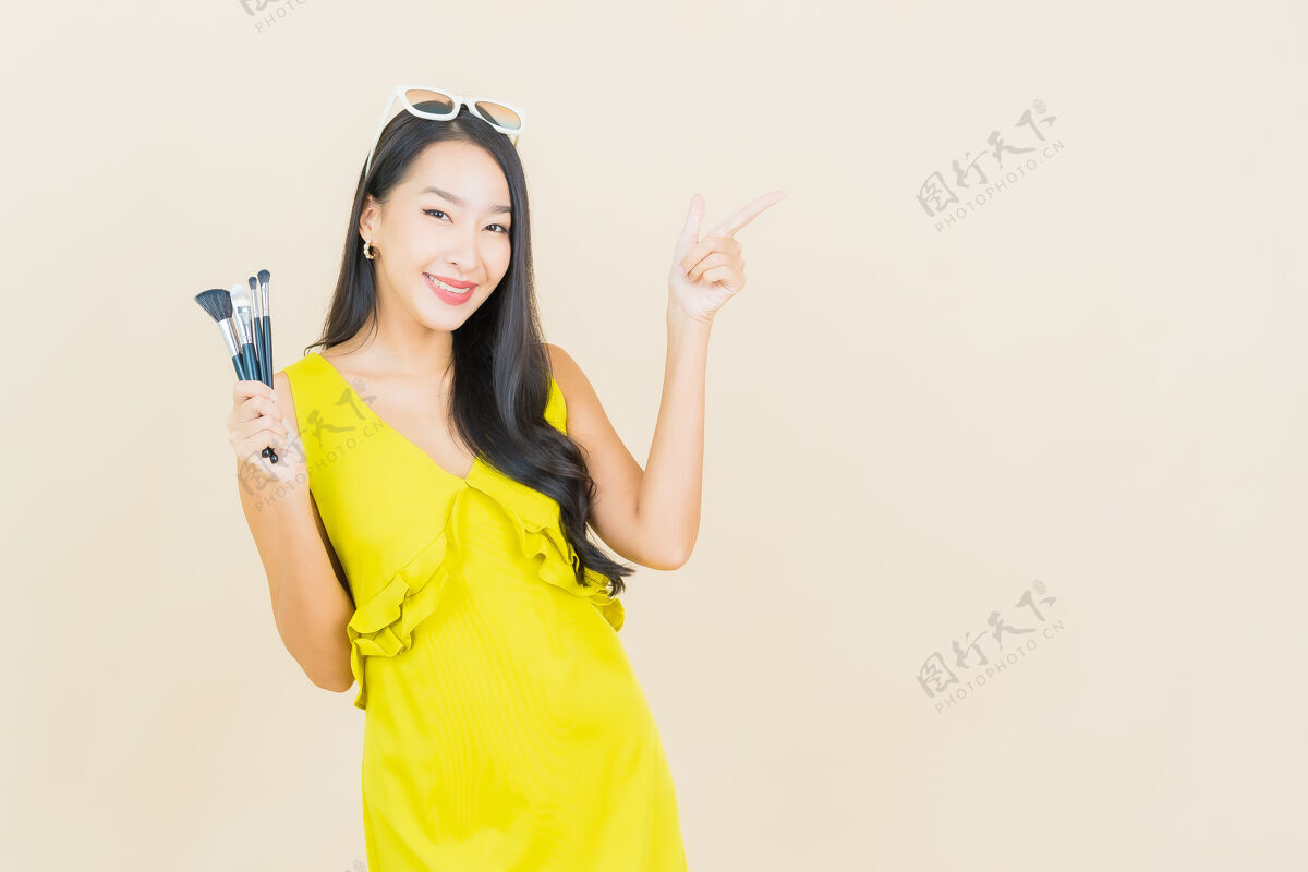媒体在彩色墙上用化妆刷描绘美丽的亚洲年轻女子女孩专业腮红