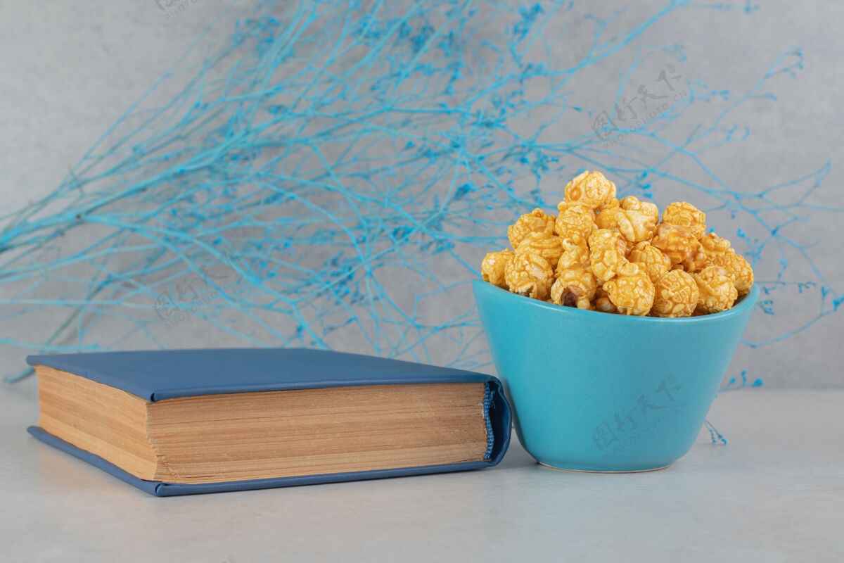 零食蓝色的树枝 一碗涂着焦糖的爆米花和一本放在大理石桌上的书外套碗树枝