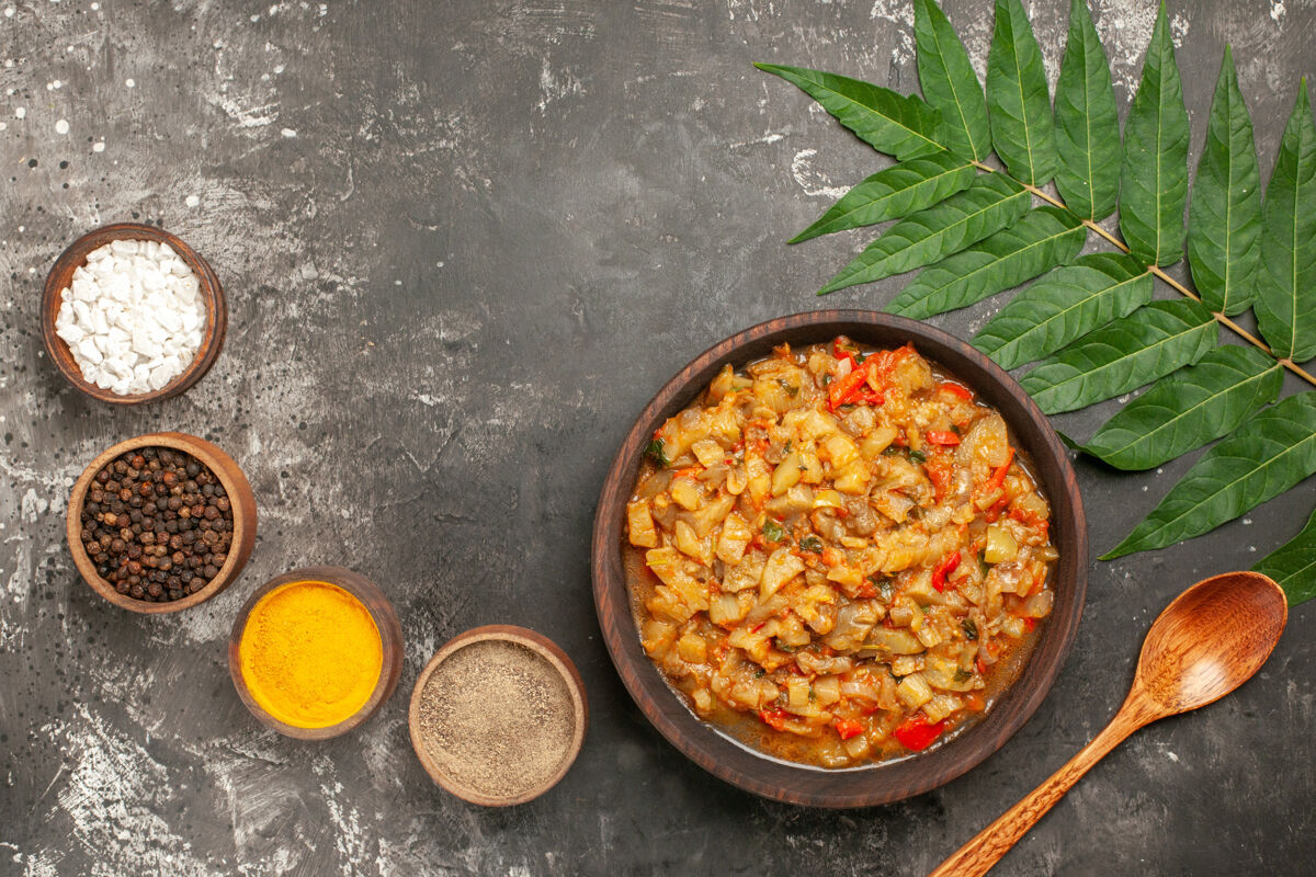 碗顶视图烤茄子沙拉在碗里 木勺 不同的香料在小碗和树叶在黑暗的表面不同茄子沙拉香料