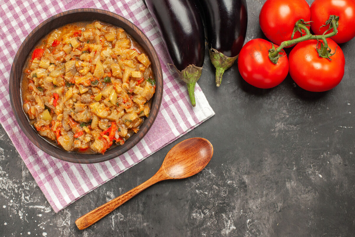 一餐顶视图烤茄子沙拉碗 木勺 西红柿和茄子在黑暗的表面木头深色食物