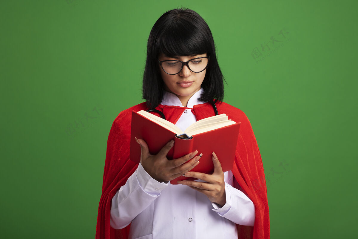 文学年轻的超级英雄女孩戴着听诊器 穿着医用长袍和斗篷 戴着眼镜 拿着书看欢呼现代女人