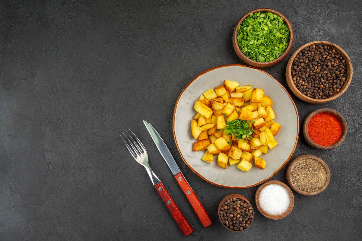盘子美味的炸土豆在黑暗的表面与绿色和调味品盘子内俯视图调味品果仁农产品