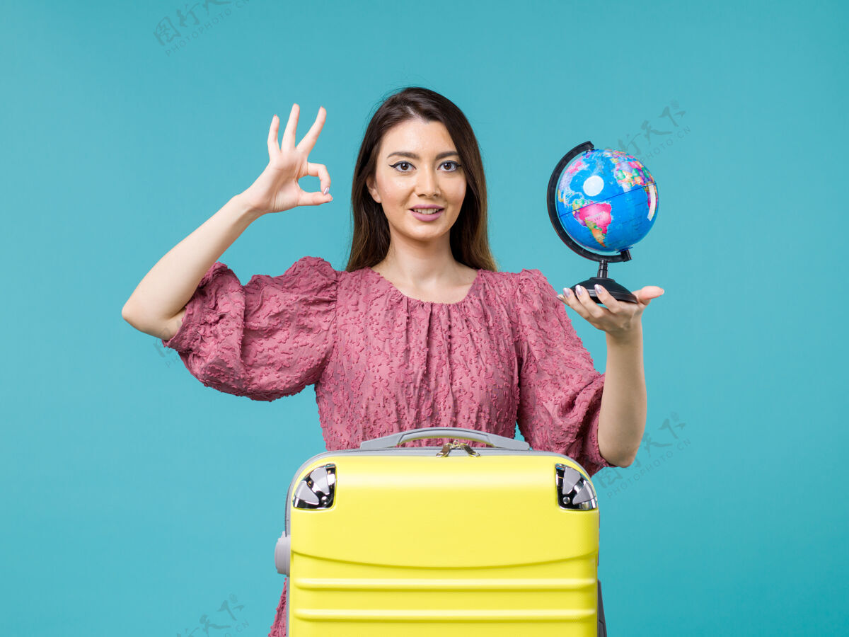 地球前视度假中的女性手持蓝色背景的地球仪出海度假旅行避暑的女性前面地球风景