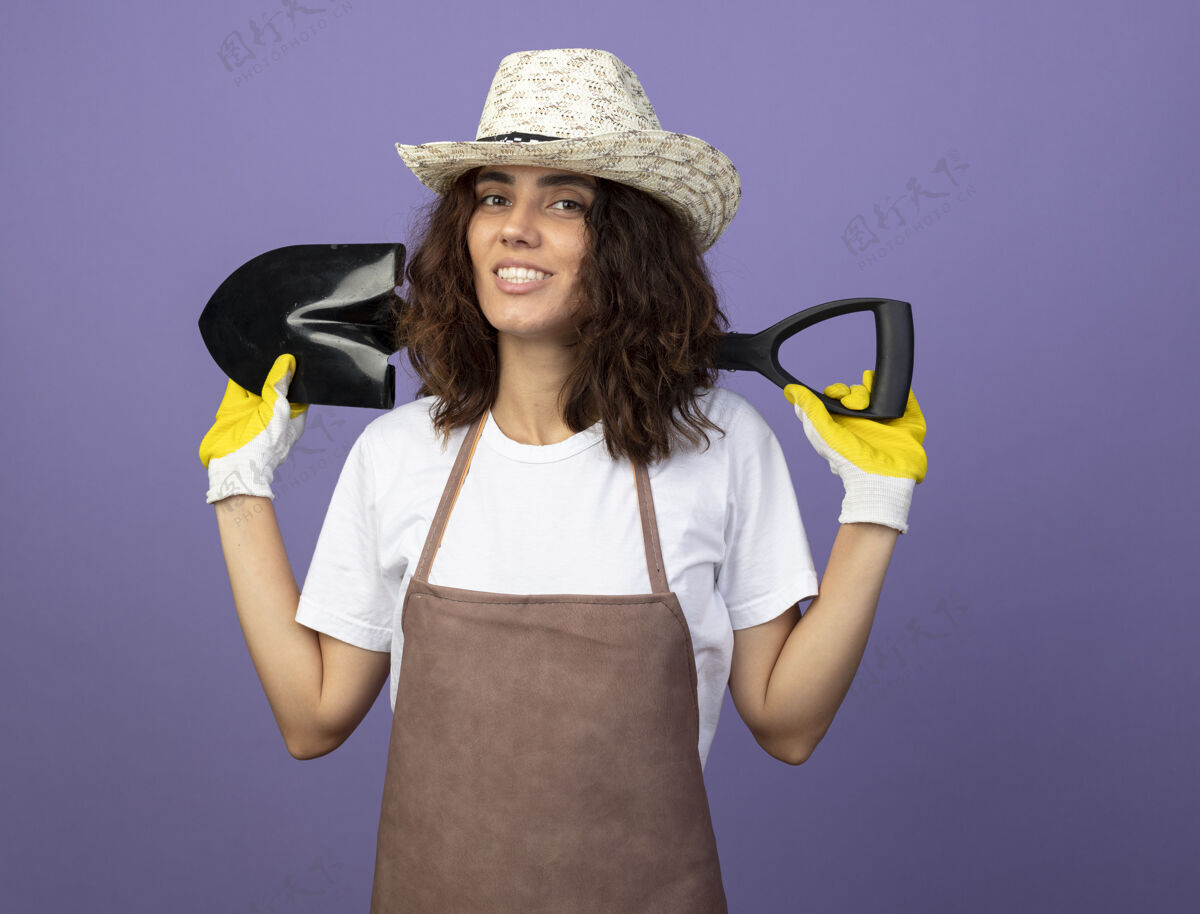 手持年轻的女园丁面带微笑 穿着制服 戴着园艺帽和手套 肩上扛着铲子黑桃制服紫色