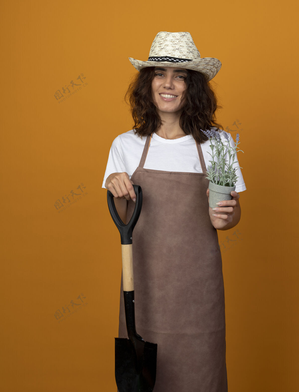 微笑身着制服的年轻女园丁微笑着 戴着园艺帽 手里拿着花盆里插着花的铁锹花盆穿黑桃
