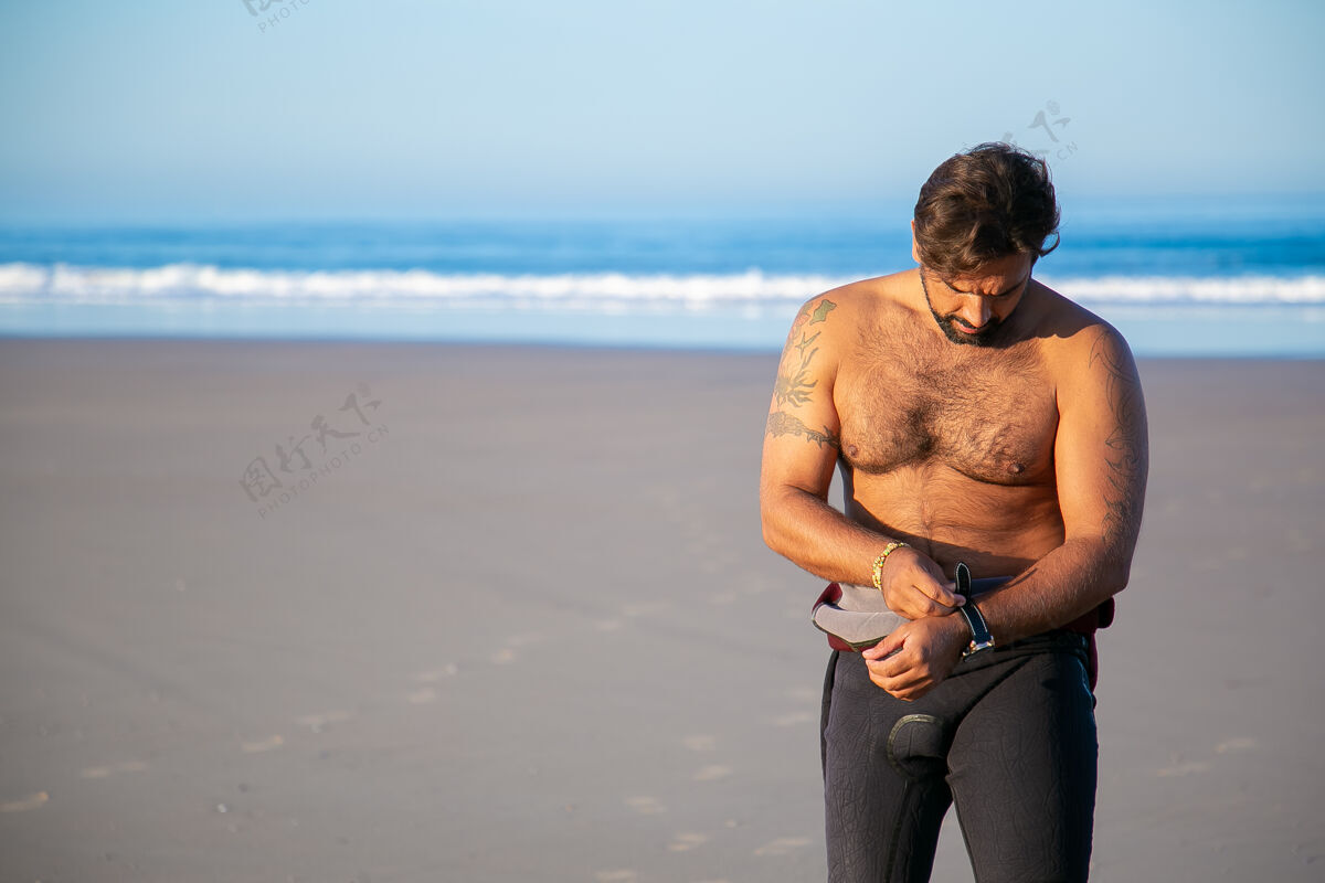 站立运动员穿上潜水衣在海边冲浪 然后脱下手表手表穿上男人