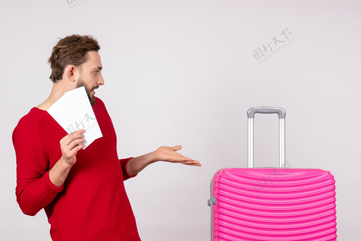球员正面图：年轻男性 带着粉色包 手持机票 在白墙上航行 飞行 彩色旅行 旅游度假 照片情感景观年轻男性情绪