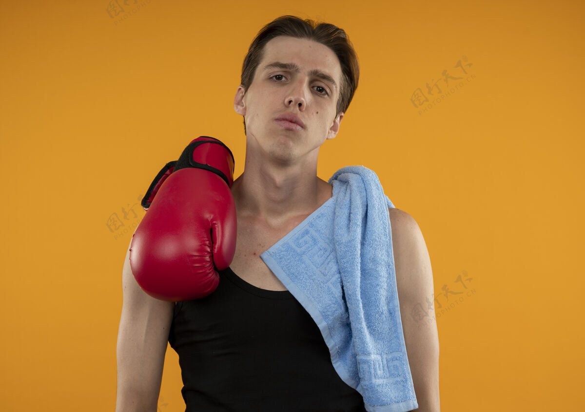 年轻年轻的运动型男人 肩上戴着毛巾和拳击手套 孤零零地站在橙色的墙上毛巾手套肩膀