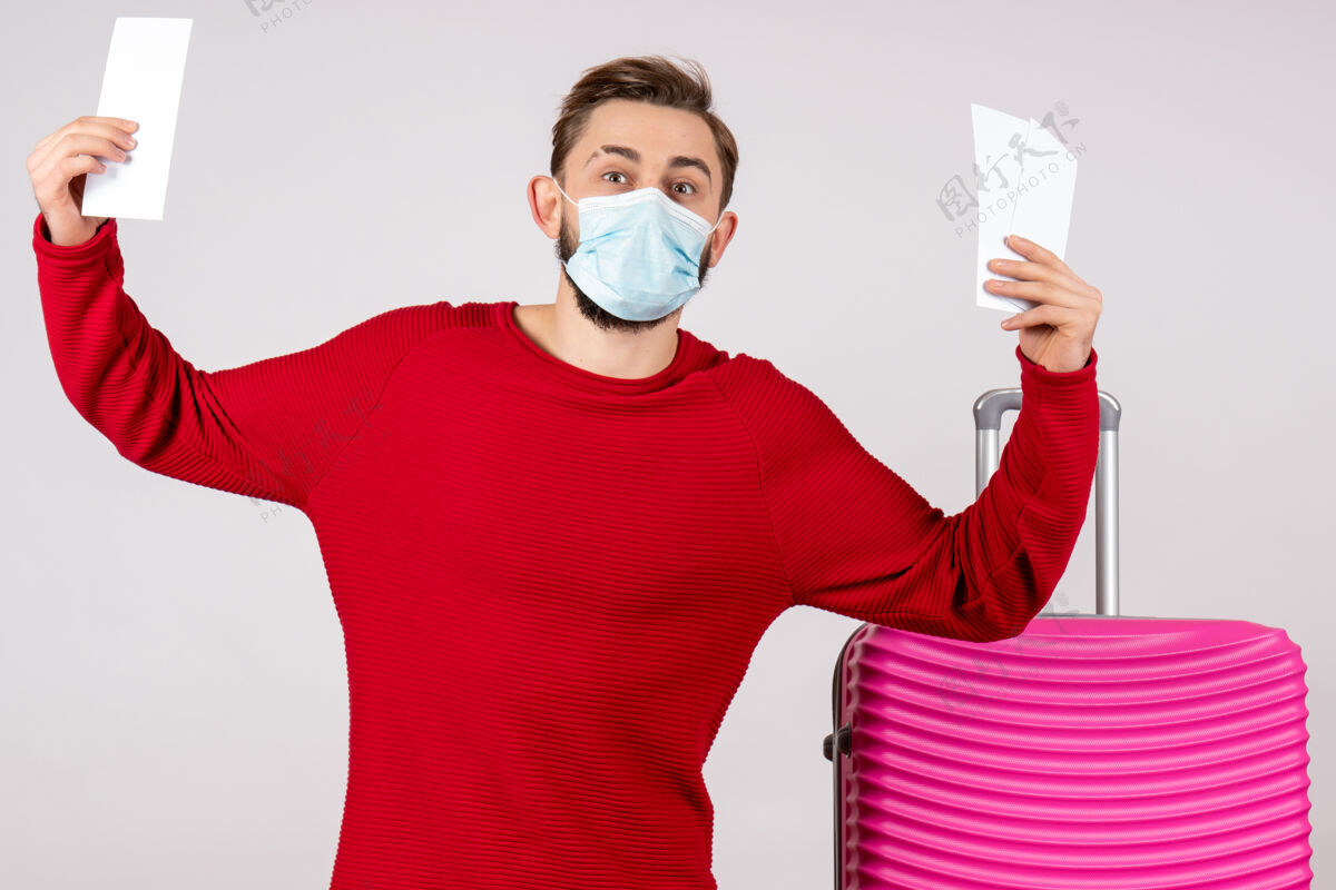 成人正面图年轻男性戴着无菌口罩拿着机票在白墙上航行covid-航班旅行度假彩色情感病毒胡子情绪病毒