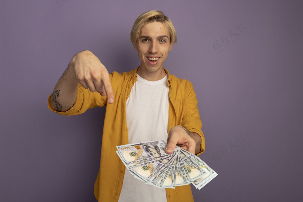 穿微笑着直视前方穿着黄色t恤的年轻金发男子拿着 指着紫色的钞票 留着复印空间黄色金发家伙