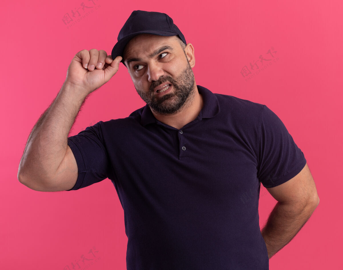 拿着一个穿着制服 戴着帽子的中年送货员被隔离在粉红色的墙上送货男人不愉快