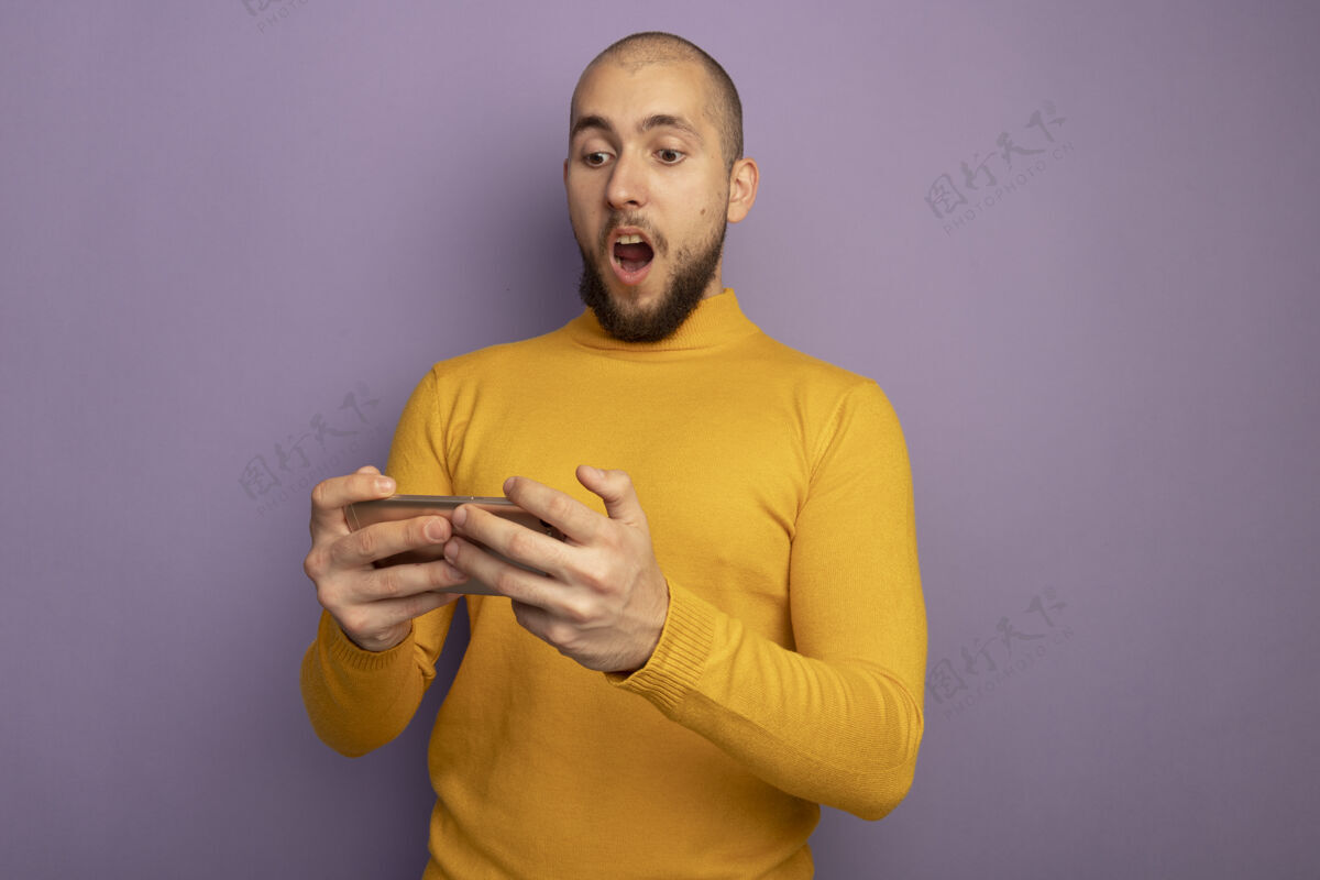 年轻人惊讶的年轻帅哥抱着手机看着孤立的紫色电话成年人伙计