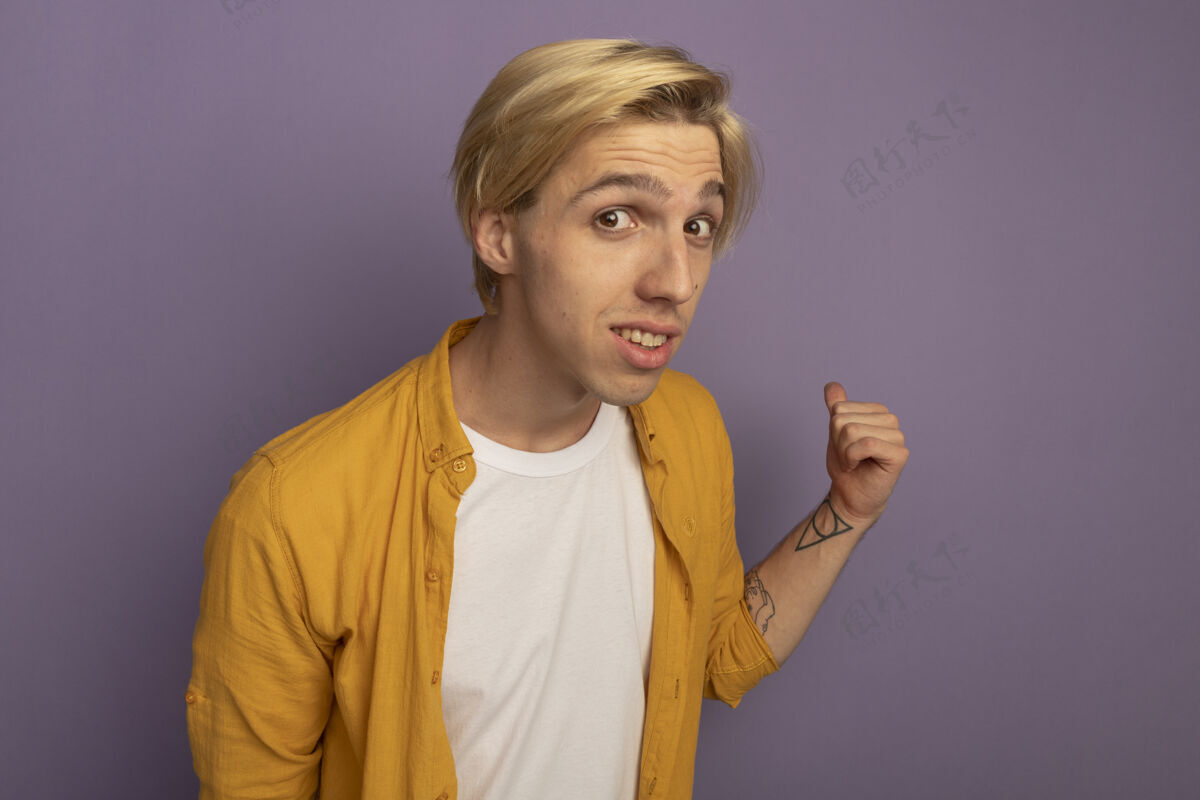 紫色印象深刻的年轻金发男子穿着黄色t恤点在后面孤立的紫色与复制空间金发穿着尖