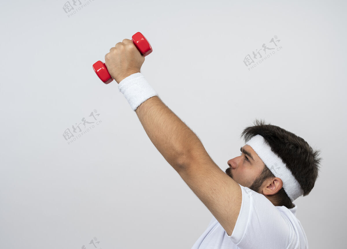 拉美裔紧张的年轻运动型男子站在侧视图戴着头带和腕带锻炼与哑铃隔离在白色与复制空间人随便