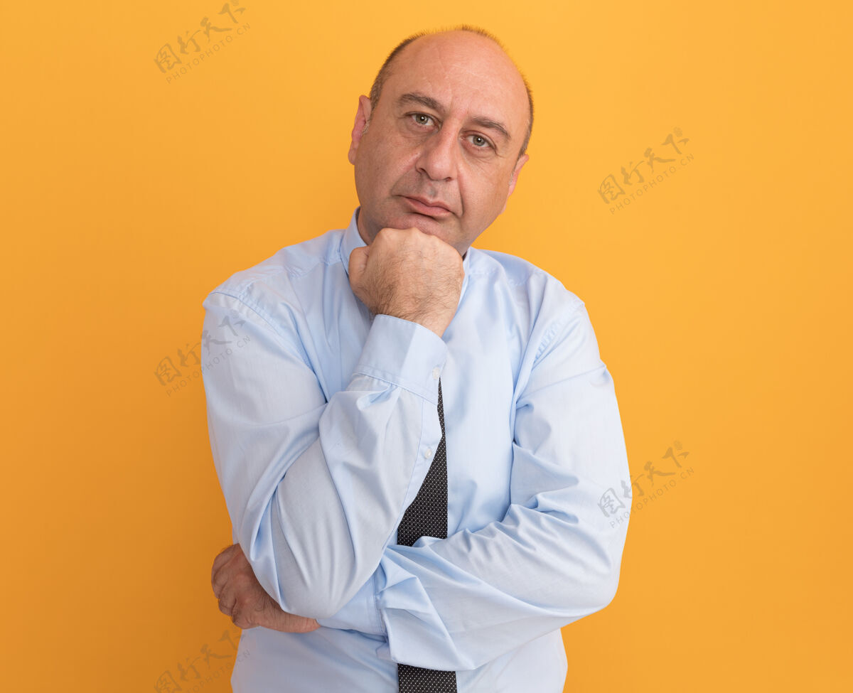 中年自信的中年男子穿着白色t恤打着领带把拳头放在下巴下孤立在橙色的墙上下巴拳头男人