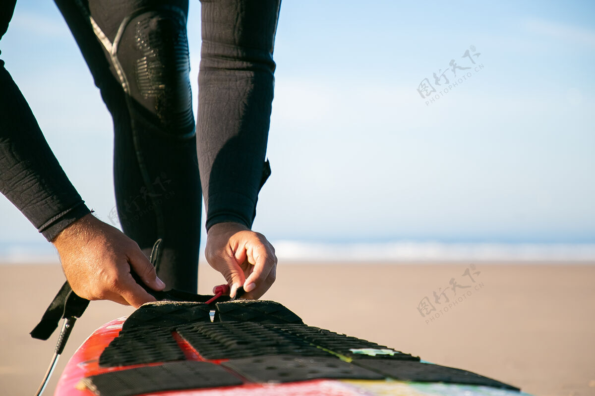 水在海边 穿着潜水服的冲浪者用手把冲浪板绑在脚踝上透明特写人