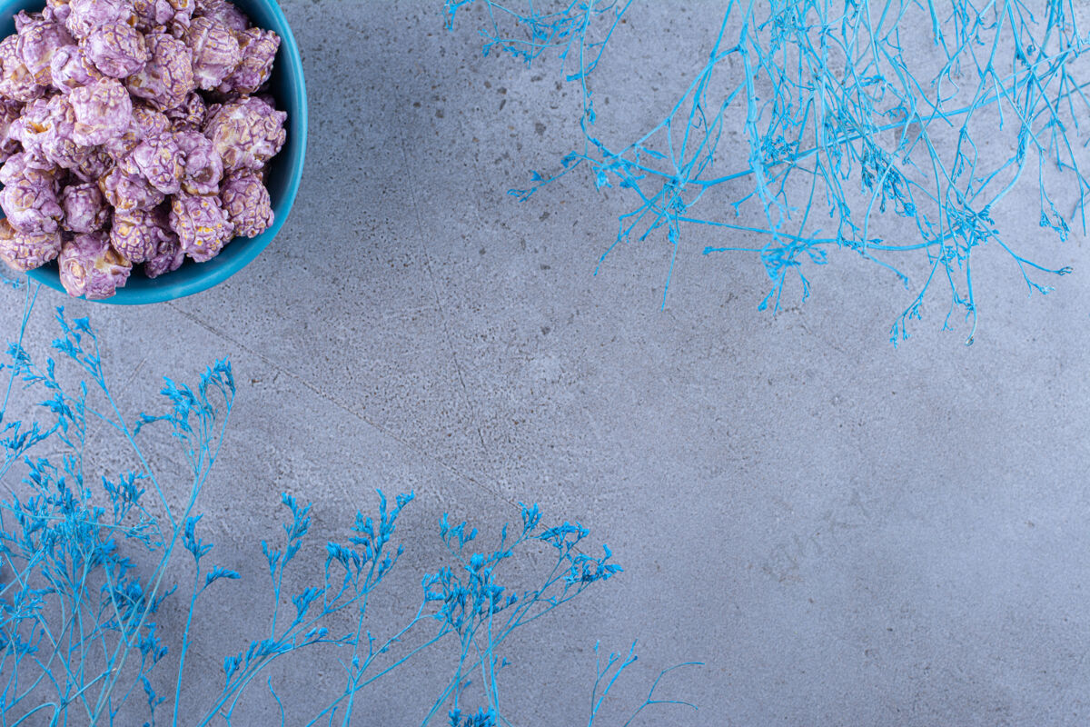 糖果蓝色的爆米花糖碗旁边是大理石表面的蓝色装饰树枝树枝碗玉米