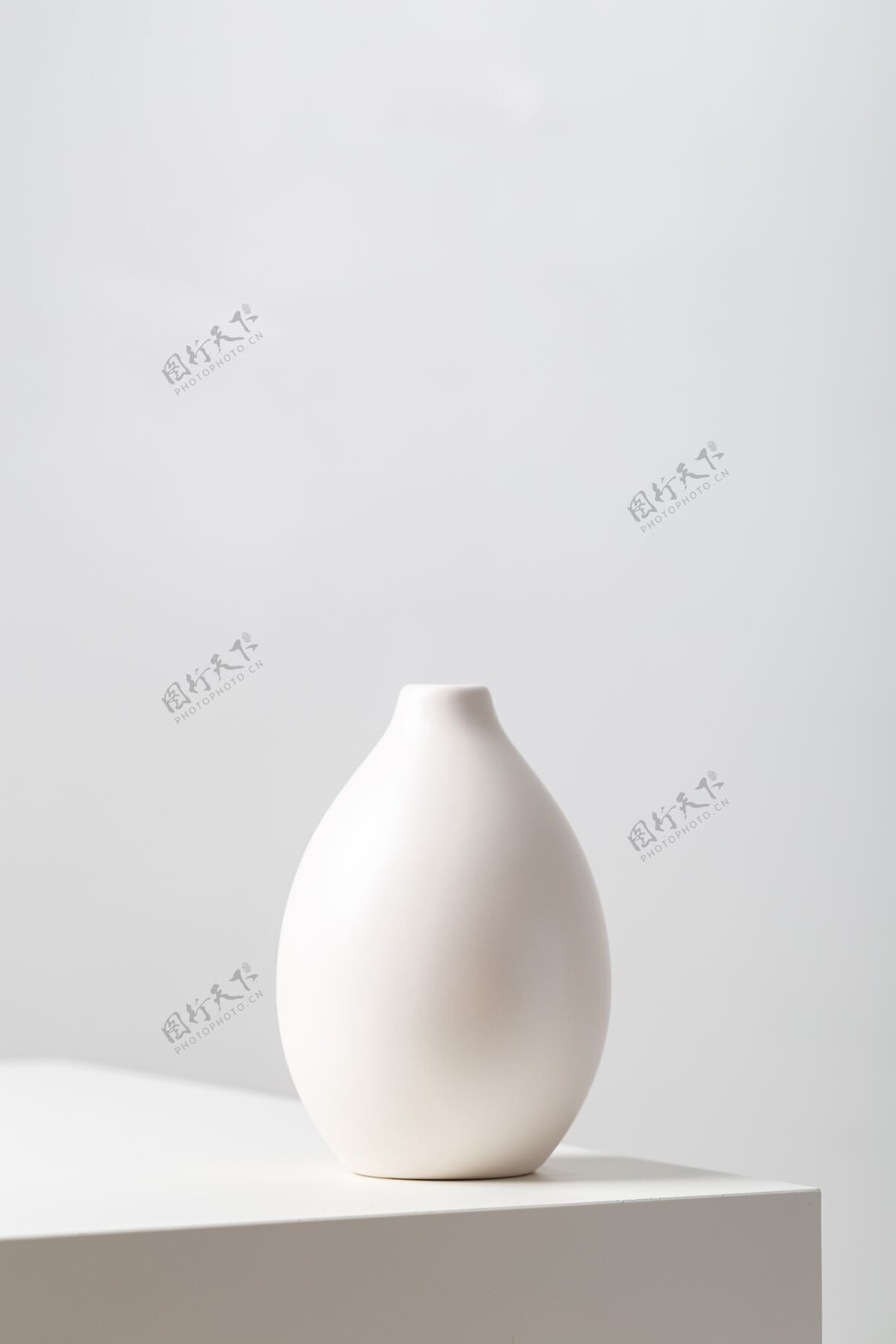 灯垂直特写一个白色的粘土花瓶在桌子上的灯光下映衬着一个白色的陶瓷空白容器
