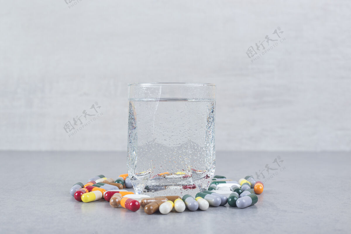 片剂一杯纯水 灰色背景上有五颜六色的药丸背景色彩清晰