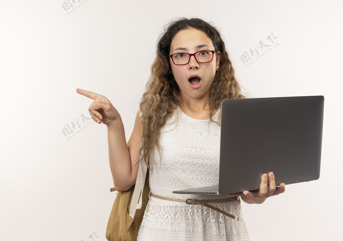 持有印象深刻的年轻漂亮的女学生戴着眼镜 背着手提电脑 指着隔离在白色的一边印象壁板包