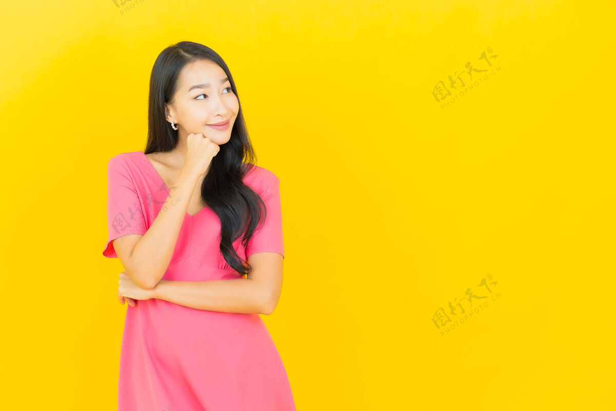 充满活力黄色墙壁上 美丽的亚洲年轻女子身着粉色连衣裙微笑的画像模型人明亮