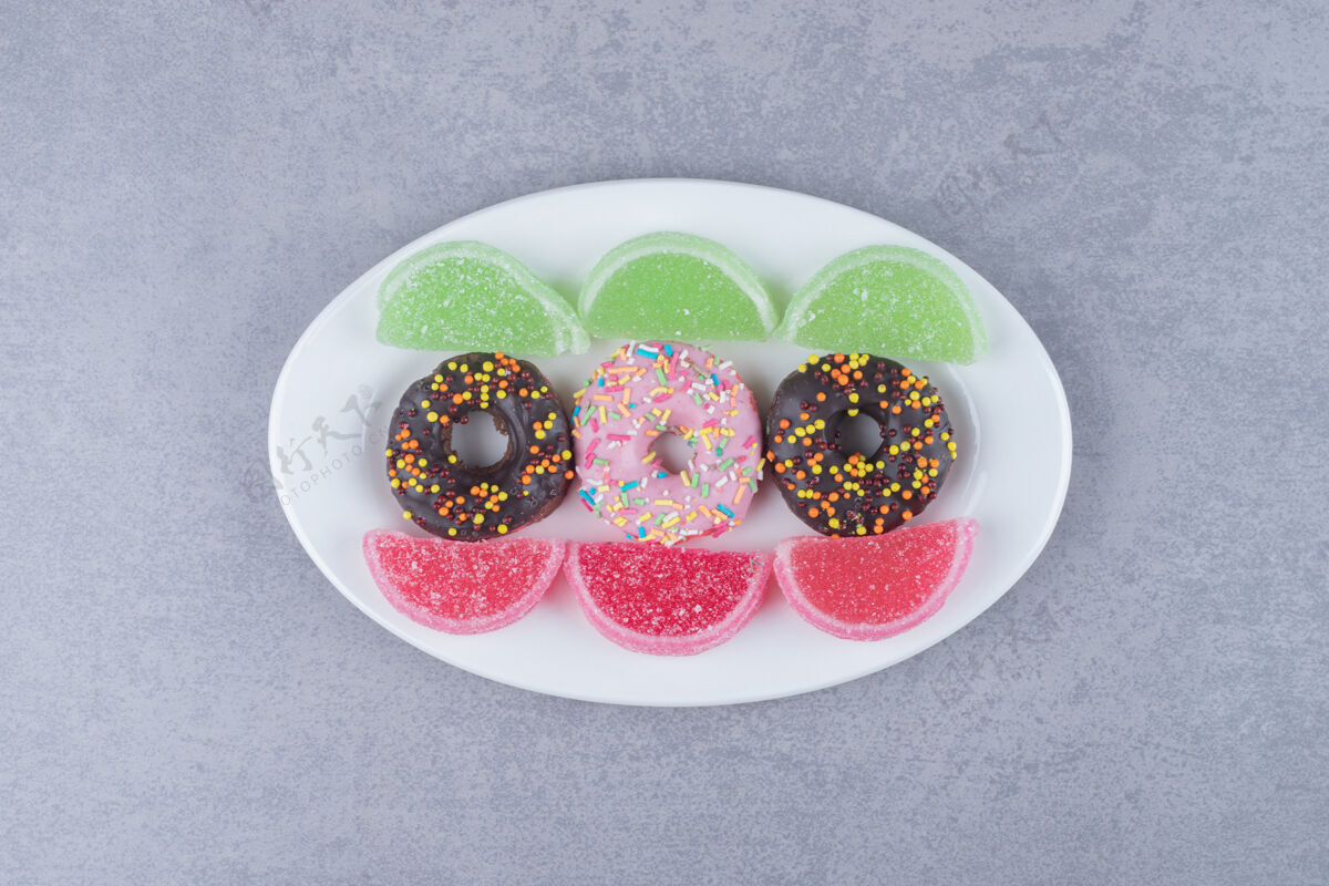 洒在大理石表面的盘子上放着一排的甜甜圈和果酱糖釉面甜点