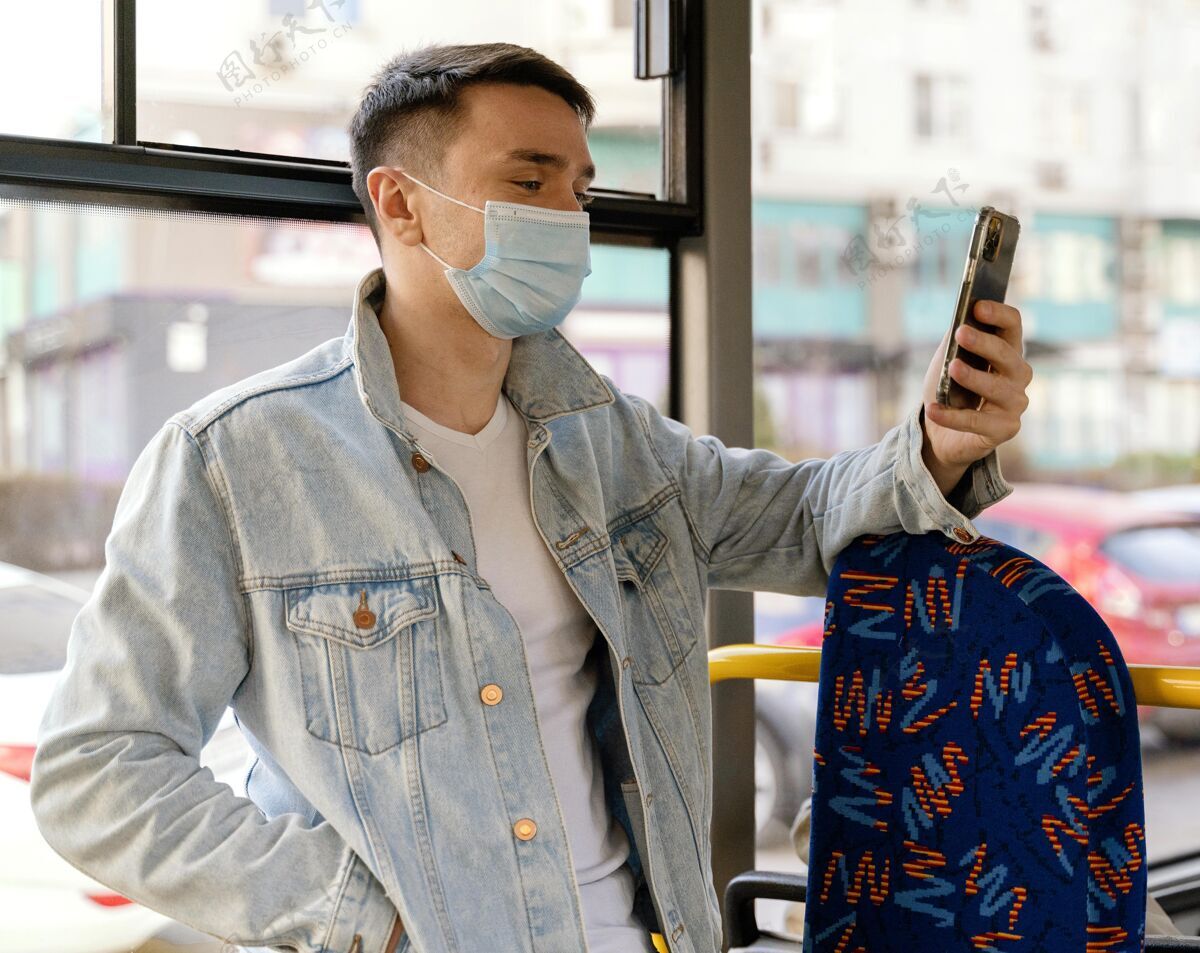 男人年轻人乘坐城市巴士使用智能手机外科口罩病毒防护口罩