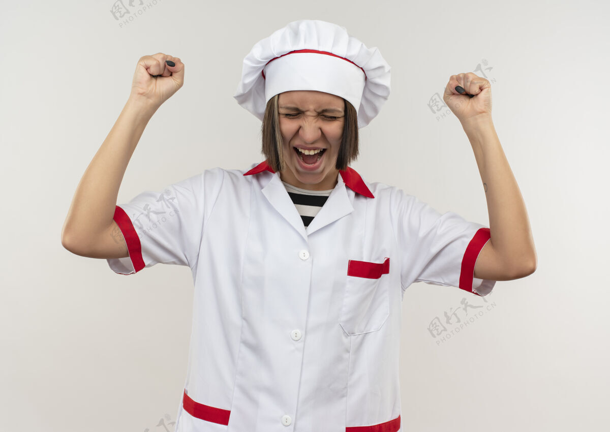 封闭快乐的年轻女厨师穿着厨师制服举起拳头闭上眼睛孤立在白色眼睛烹饪提高
