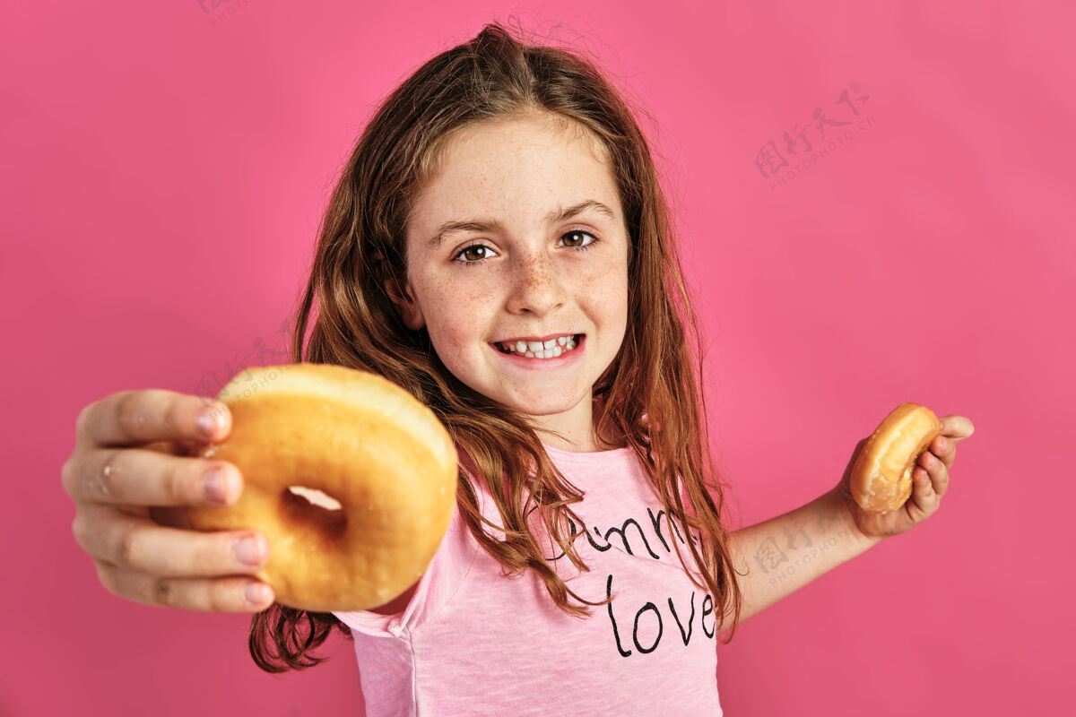 白种人一个小女孩在粉红色背景上提供甜甜圈的肖像甜甜圈人提议