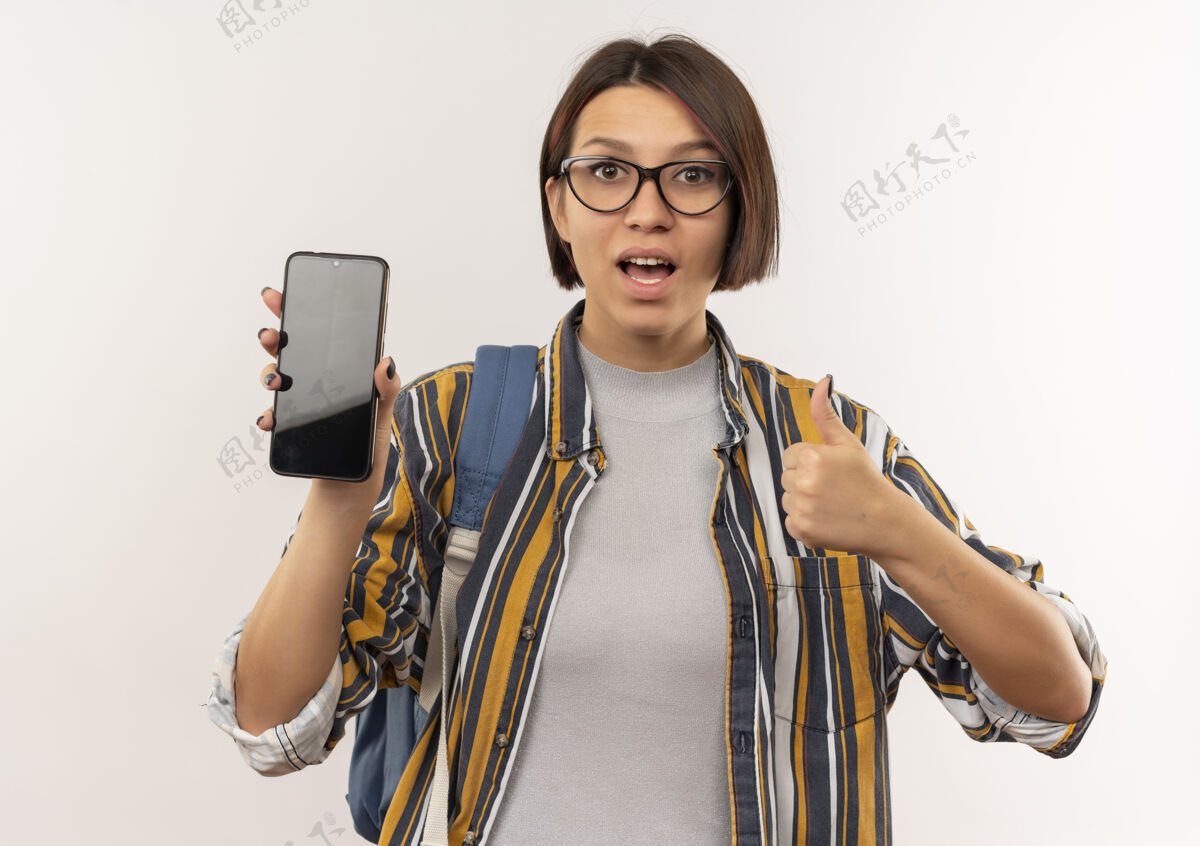 学生印象深刻的年轻女学生戴着眼镜 背着书包 展示着手机和大拇指 孤立地站在白色上展示包眼镜