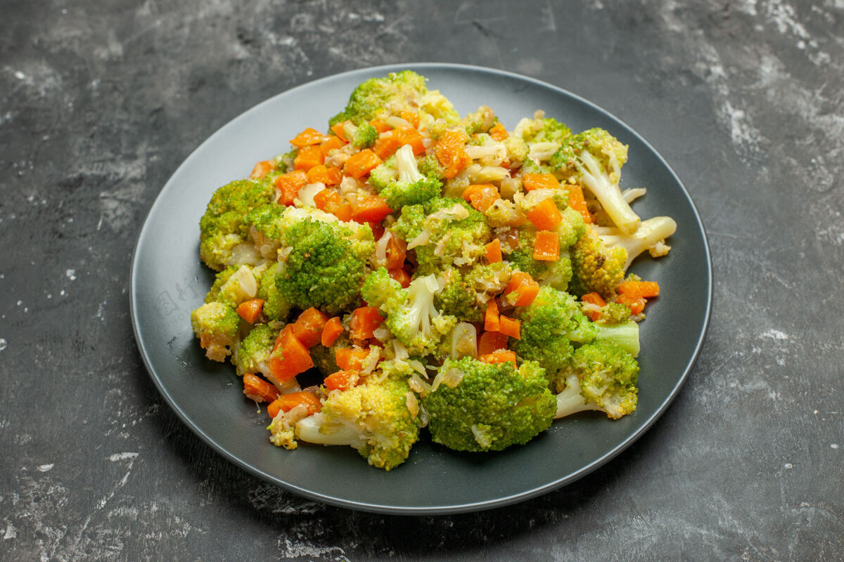 午餐在灰色桌子上的黑色盘子上放半杯健康的西兰花和胡萝卜健康一半花椰菜