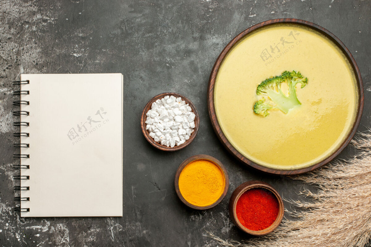 食物奶油西兰花汤在一个棕色的碗和不同的香料与笔记本在灰色的桌子上碗笔记本健康