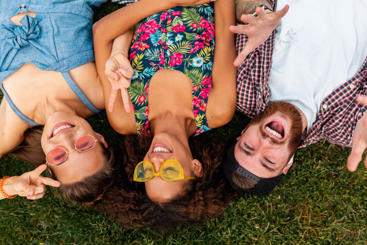 女人俯瞰五颜六色时尚快乐的年轻朋友们躺在公园的草地上 男女同乐团结多样性在一起