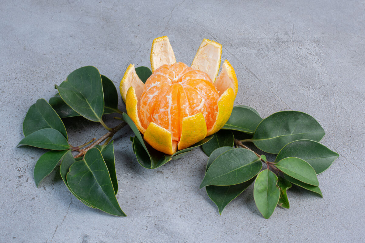 新鲜剥皮的橘子和大理石背景上的装饰叶饮食健康美味