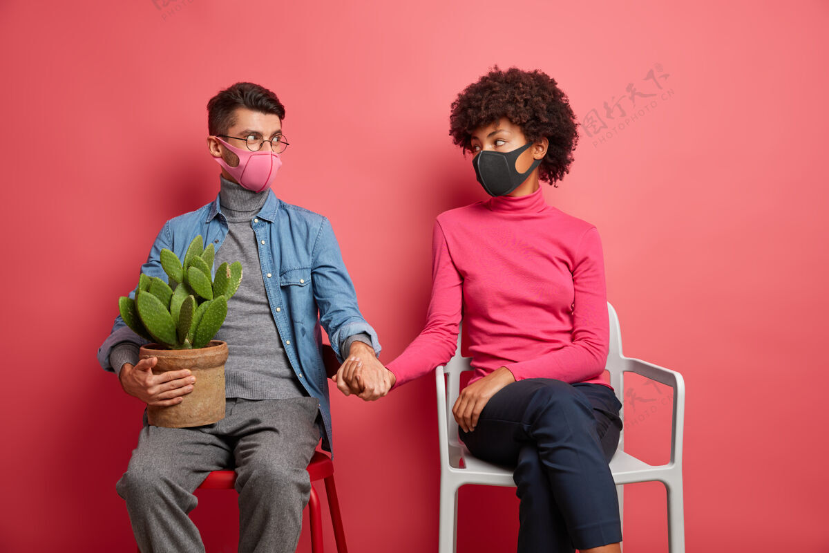 医疗严重感染冠状病毒的夫妻互相搀扶手戴防护面罩坐在椅子上穿休闲服在家度过时光室内丈夫美国