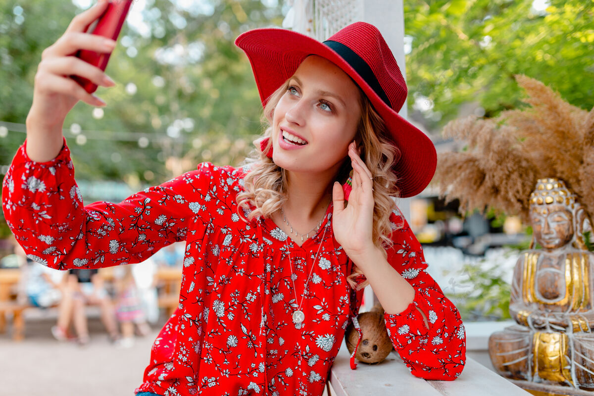 外面迷人的时尚金发微笑的女人在稻草红色帽子和衬衫夏季时尚服装拍照自拍智能手机咖啡厅配件脸金发