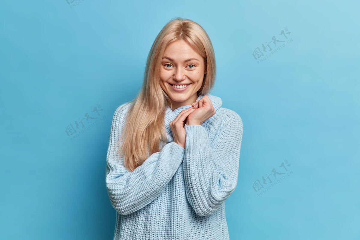 情感快乐羞涩的少女画像双手合十神采奕奕 穿着休闲针织衫对着蓝色的墙壁摆姿势人满意衣领