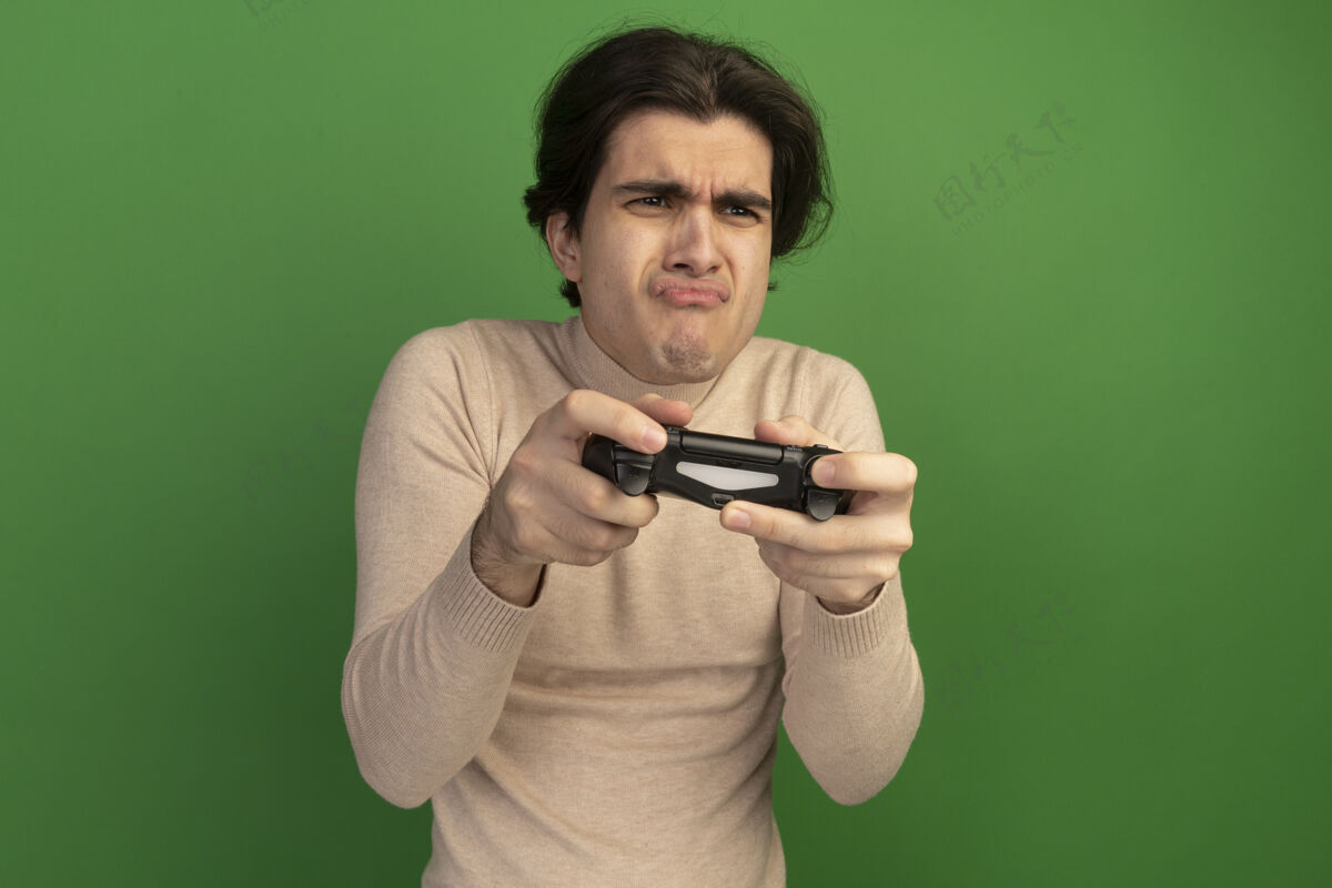 不愉快不高兴地看着身边年轻帅哥拿着游戏控制器操纵杆孤零零地站在绿色的墙上游戏控制器家伙